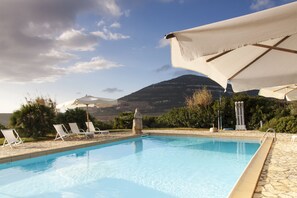 Une piscine entourée de chaises longues et de parasols, avec une végétation luxuriante et des montagnes en toile de fond.