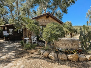 A rustic reception area with a stone wall, a wooden building, and outdoor seating. - Tenute San Giuliano (Alghero)
