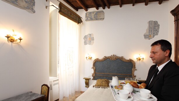 A hotel room with a bed, a bedside table, a chair, and a tray with breakfast items. - Navona Governo Vecchio (Rome)