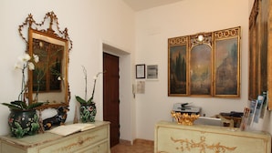 A room with a wooden door, a dresser with drawers, a small table with a vase, and a large mirror with a decorative frame. - Navona Governo Vecchio (Rome)
