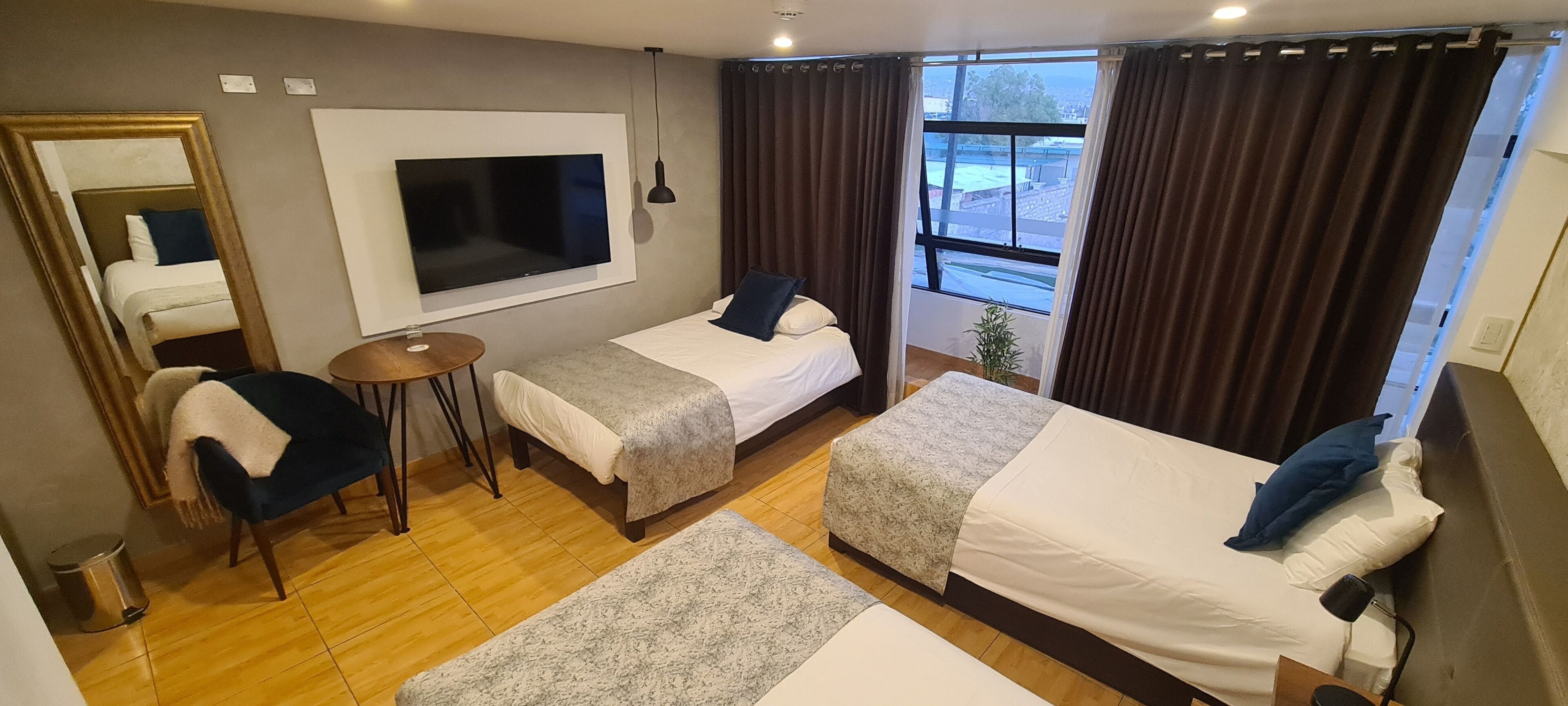 Ein Hotelzimmer mit zwei Betten, einem Fernseher, einem kleinen Tisch und einem Fenster mit Vorhängen.