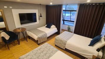 Ein Hotelzimmer mit zwei Betten, einem Fernseher, einem kleinen Tisch und einem Fenster mit Vorhängen.
