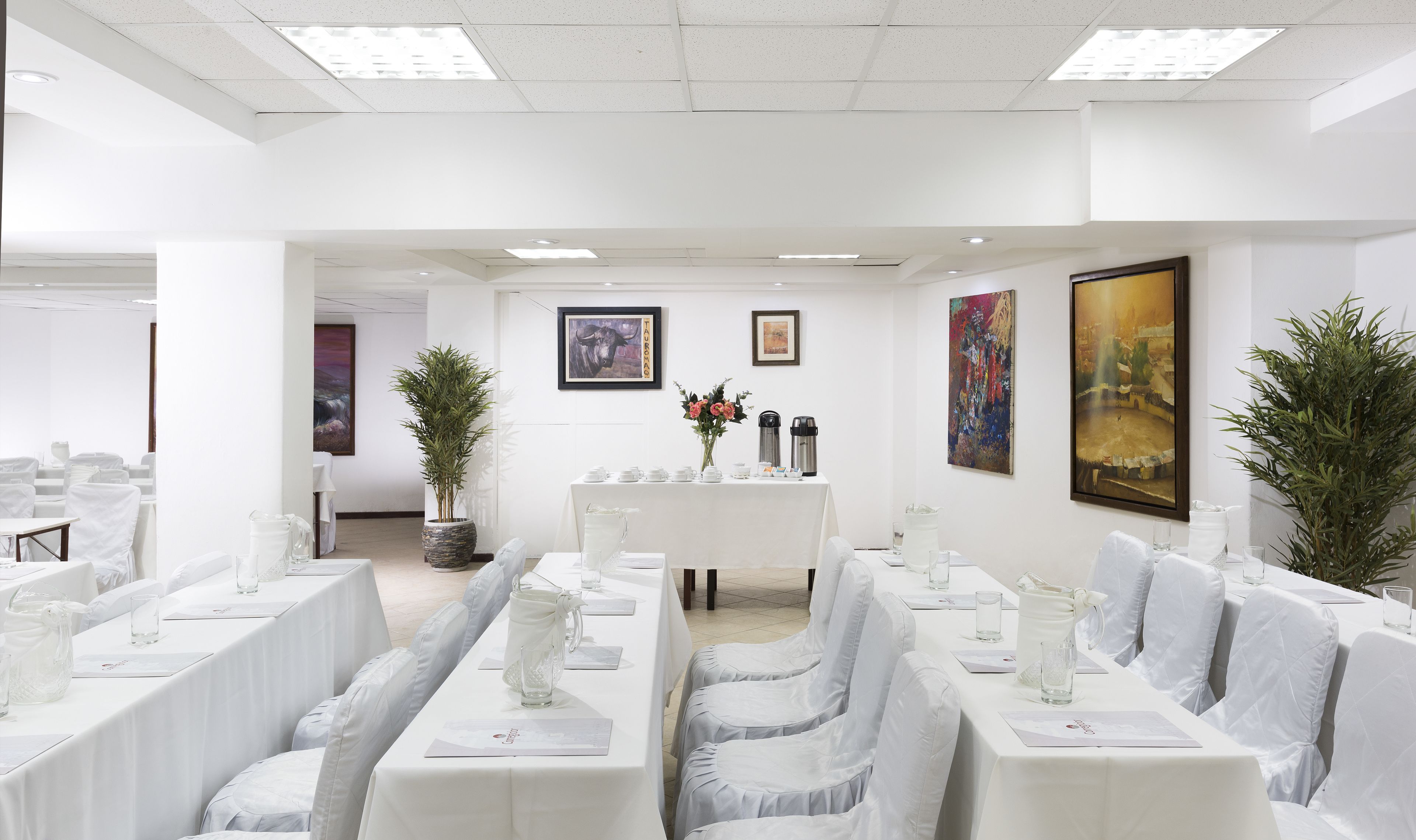 Une salle de conférence avec des tables et des chaises blanches, un coin café et des œuvres d’art accrochées aux murs.