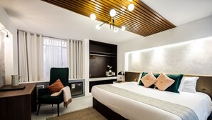 Ein modernes Hotelzimmer mit einem großen Bett, einem Schreibtisch, einem Sessel und einem fest installierten Kleiderschrank.