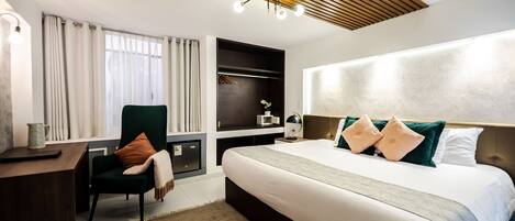 A modern hotel room with a large bed, a desk, a chair, and a built-in wardrobe.