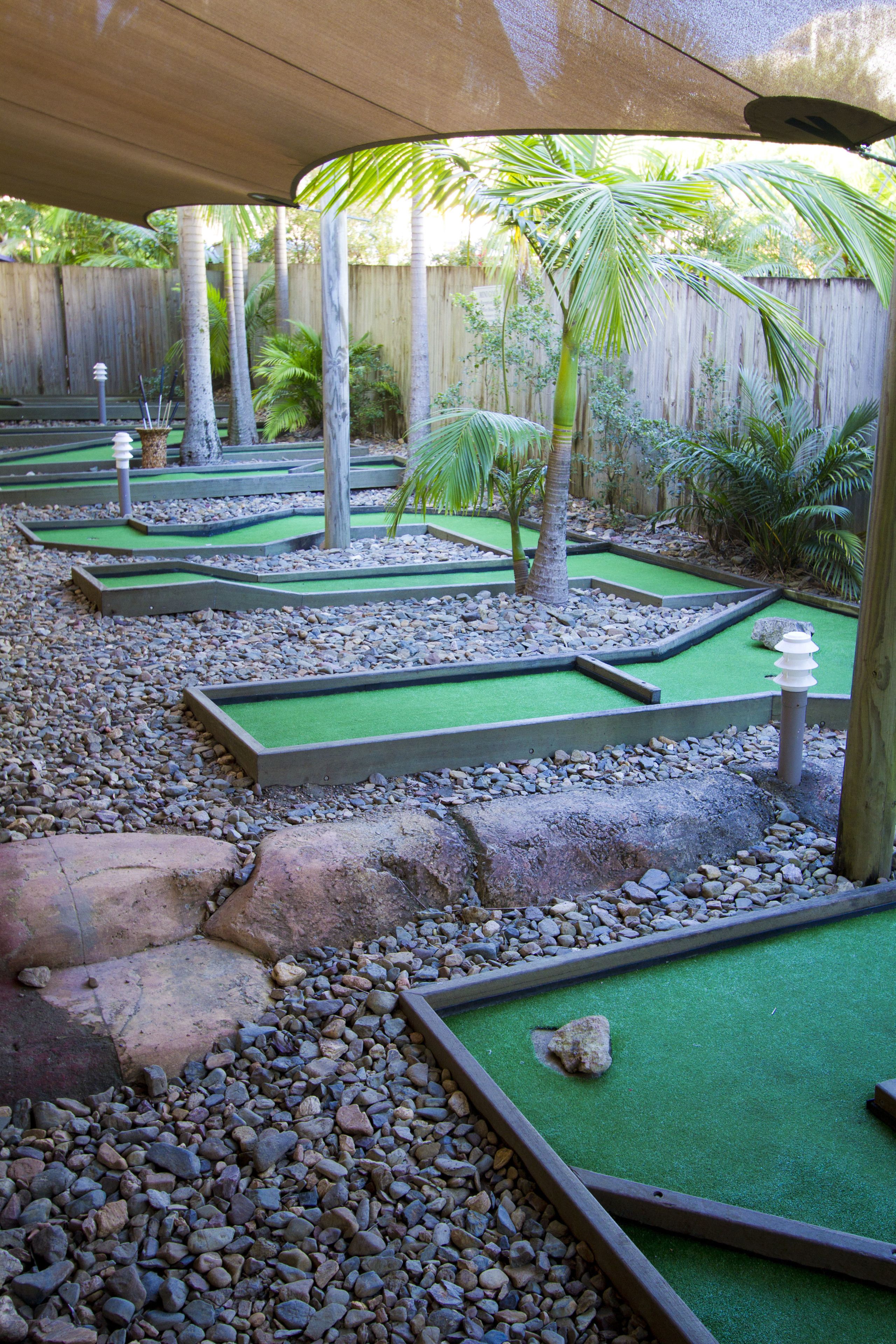 Un parcours de mini-golf doté de plusieurs zones d’entraînement au putting, entouré de graviers et de palmiers.