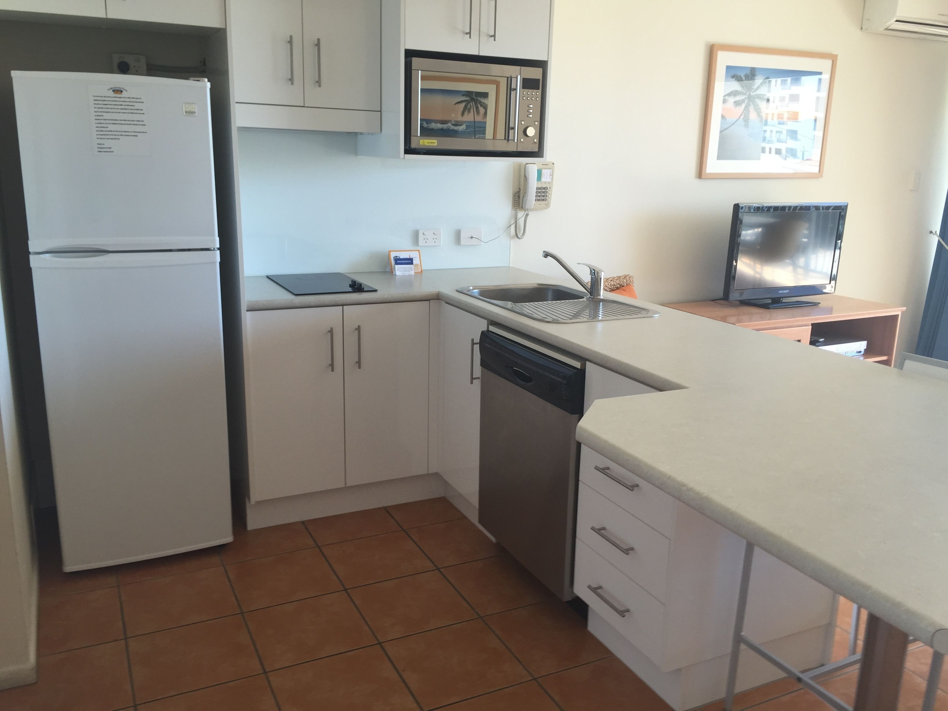 Cocina compacta con refrigerador, microondas, lavavajillas y pileta. Hay una pequeña mesada y un televisor sobre una mesa de madera.