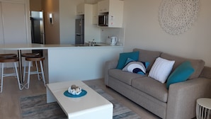 Ein modernes Wohnzimmer mit Sofa, Couchtisch und einer Küchenzeile im Hintergrund.