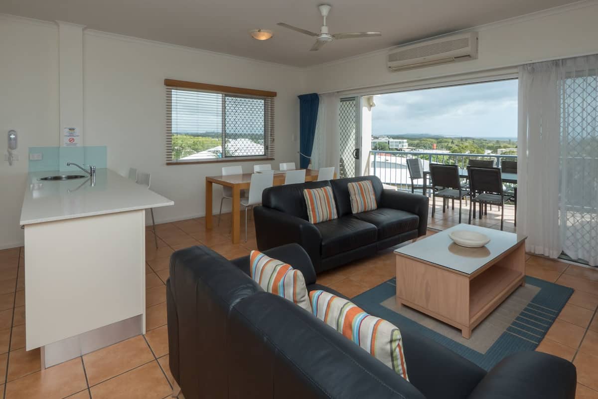 Un salon moderne avec un canapé, une table basse et un téléviseur. Il y a un balcon avec vue.