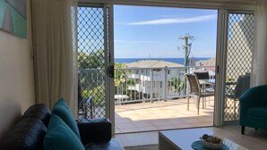 Ein Wohnzimmer mit Ledersofa, einem Couchtisch und Blick auf einen Balkon mit Gartenmöbeln und einem Gebäude im Hintergrund.
