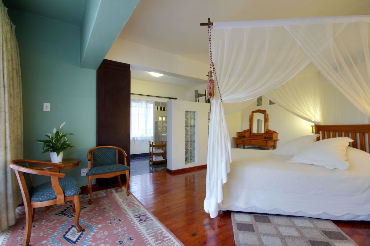 Un dormitorio con cama a dosel, una silla de madera, una mesita con una planta y una alfombra estampada.
