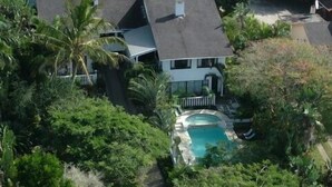 An aerial view of a house with a swimming pool surrounded by lush greenery and a palm tree.