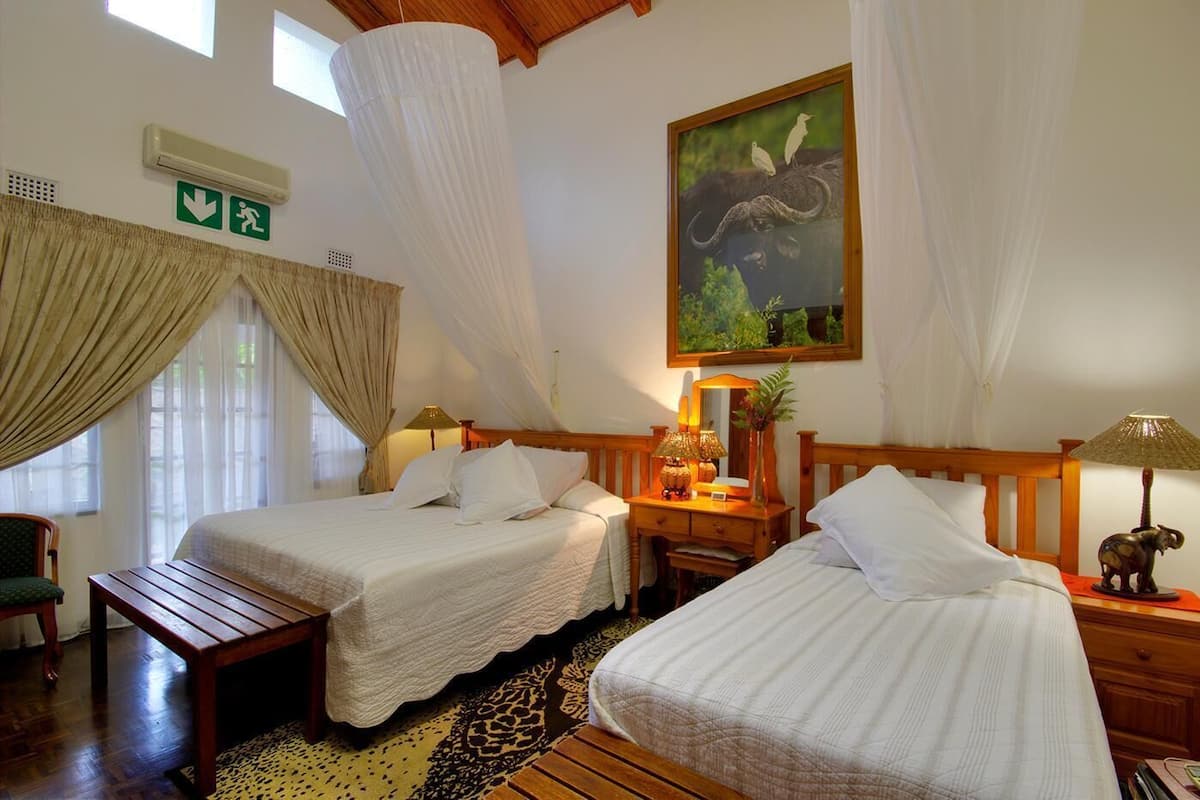 Una habitación con dos camas, una mesita de noche de madera, una lámpara, un cuadro de un búfalo y una ventana con cortinas.