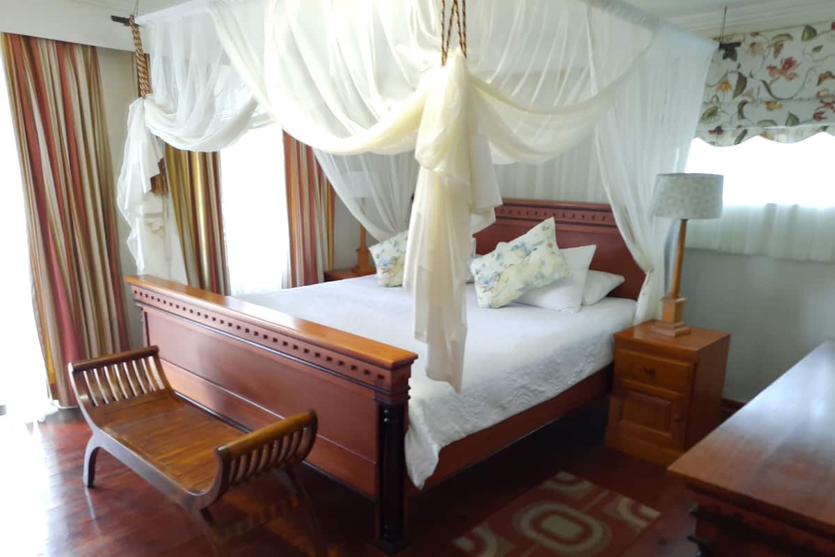 Un dormitorio con una cama de madera, una silla de madera, una mesita de noche y un mueble auxiliar.