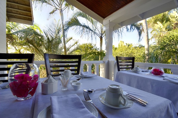 A table set for two with a white tablecloth, a glass vase with pink flowers, and a clear glass bowl.