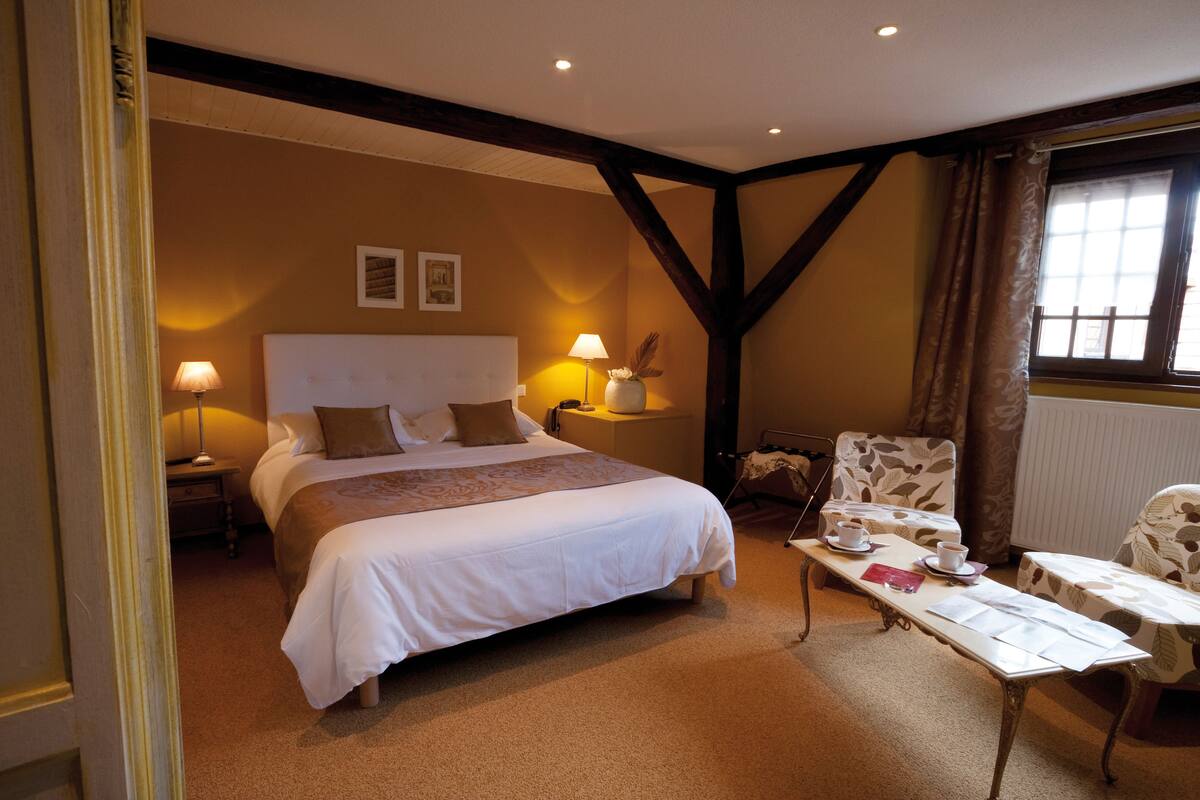 A hotel room with a large bed, bedside lamps, a table with a chair, and a window with curtains.