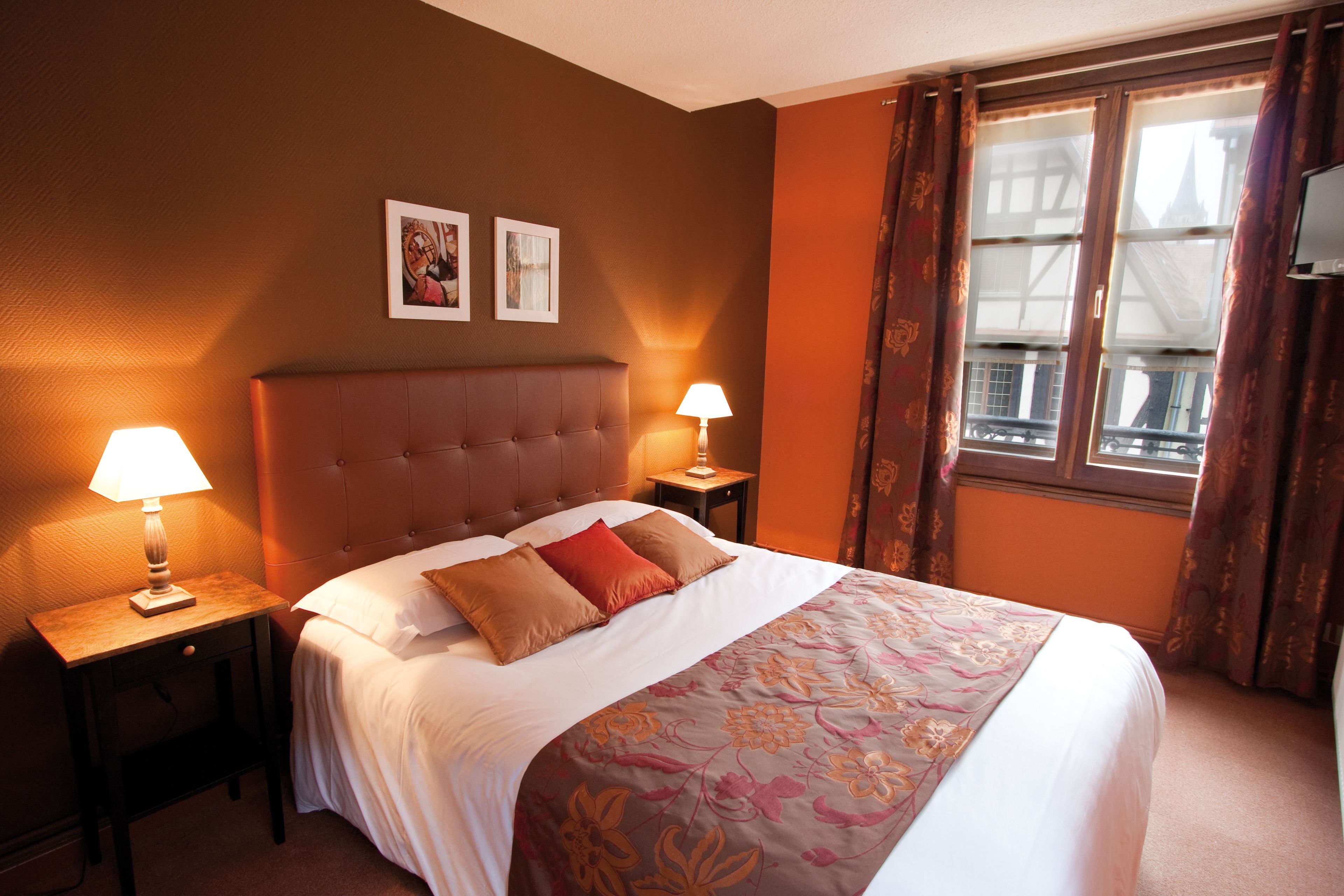 Une chambre d’hôtel avec un grand lit, deux tables de chevet avec des lampes, une tête de lit et une fenêtre avec des rideaux.