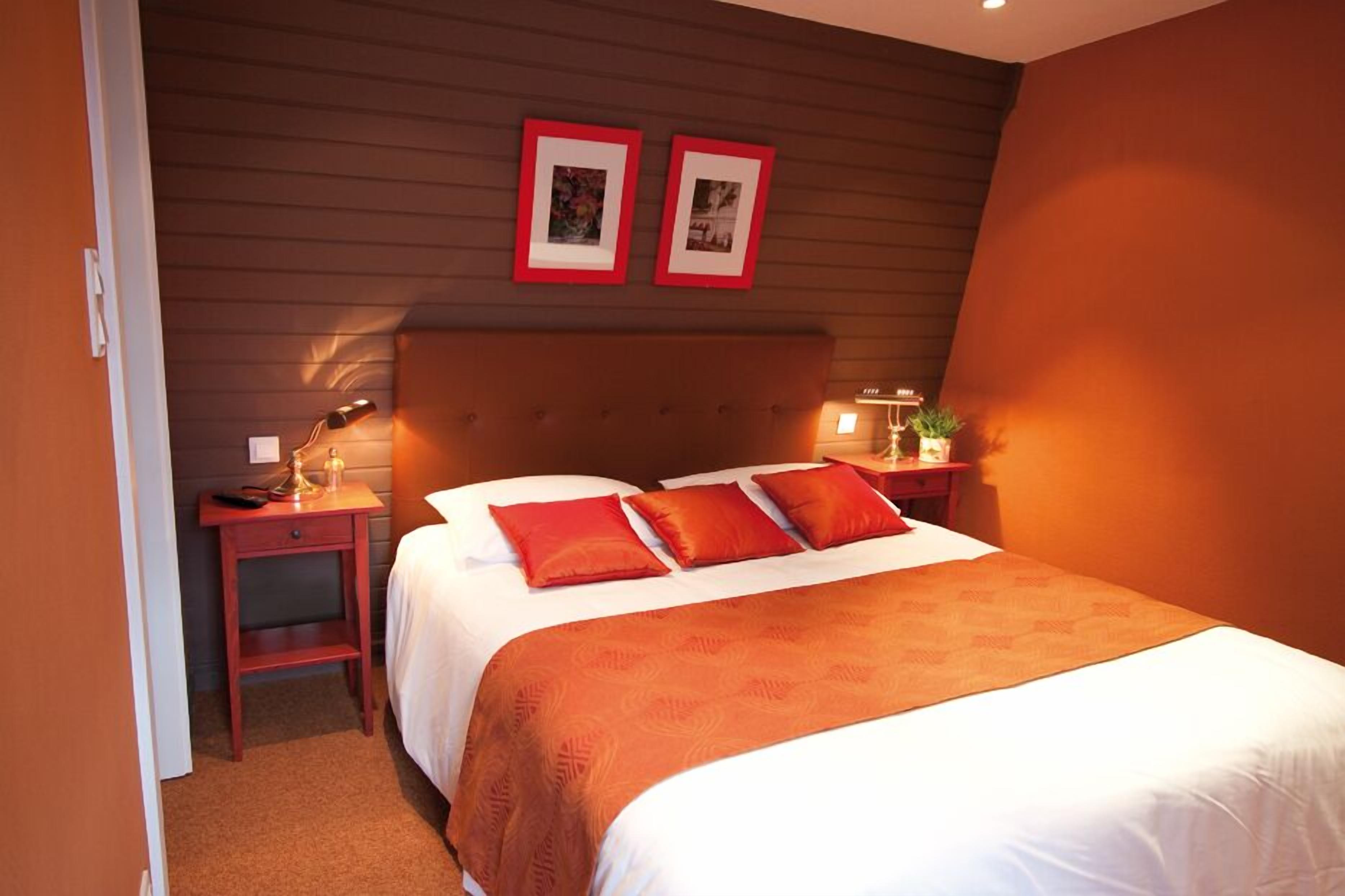 A hotel room with a large bed, two bedside tables, a nightstand, and two framed pictures on the wall.