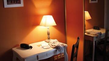 A hotel room with a desk, chair, lamp, and a mirror.