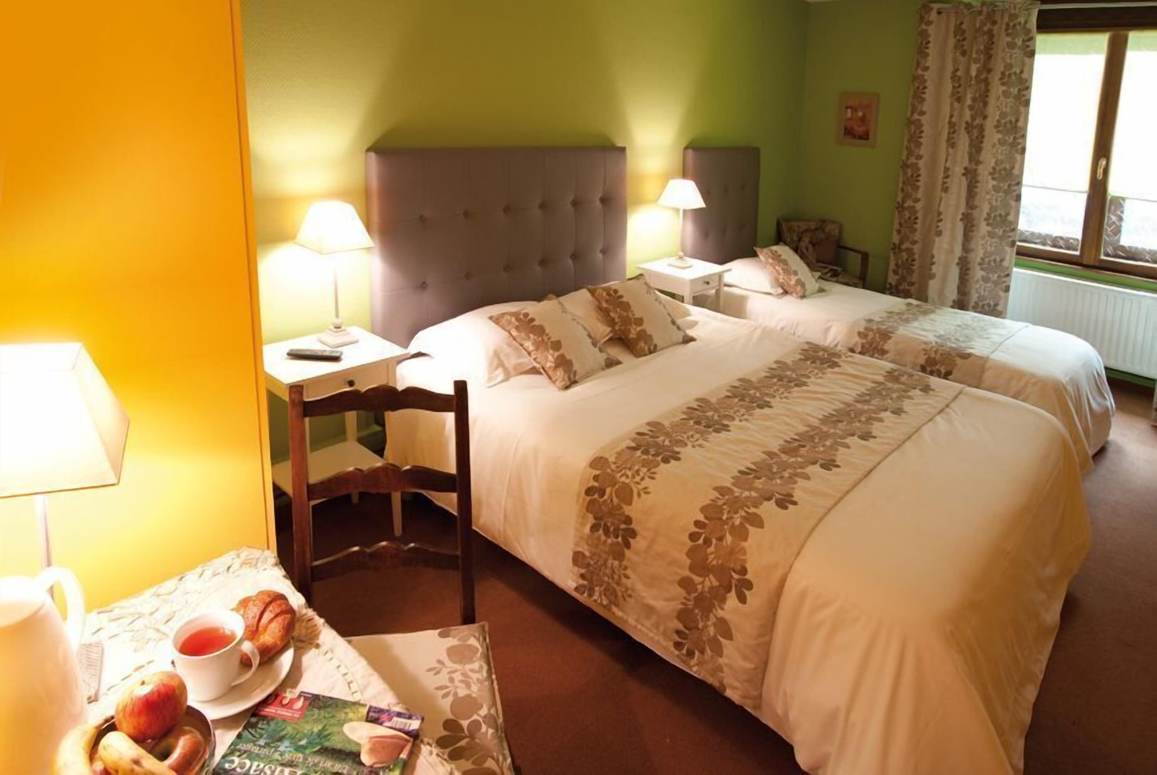 Une chambre d’hôtel avec deux lits, une chaise, une table avec des articles pour le petit-déjeuner et une fenêtre avec des rideaux.