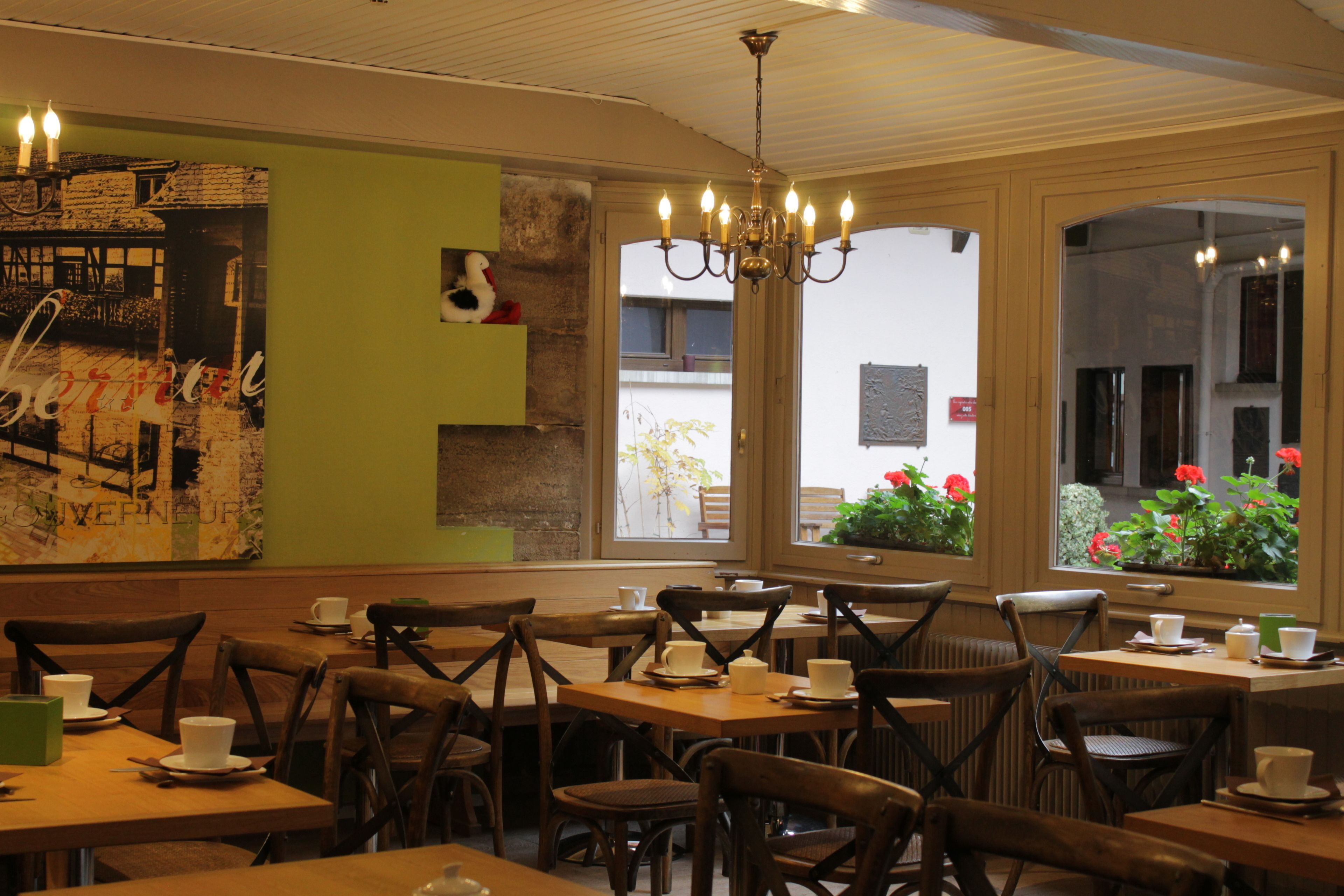 A restaurant with wooden tables and chairs, a chandelier, and a view of the street outside.