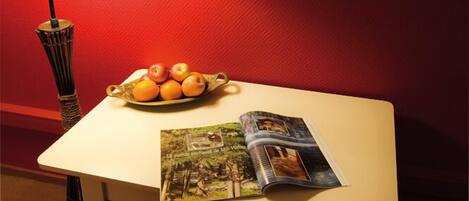 A table with a lamp, a bowl of fruit, and a magazine.