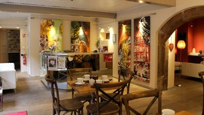 Um restaurante com mesas e cadeiras de madeira, um balcão com cardápio e arte colorida nas paredes.
