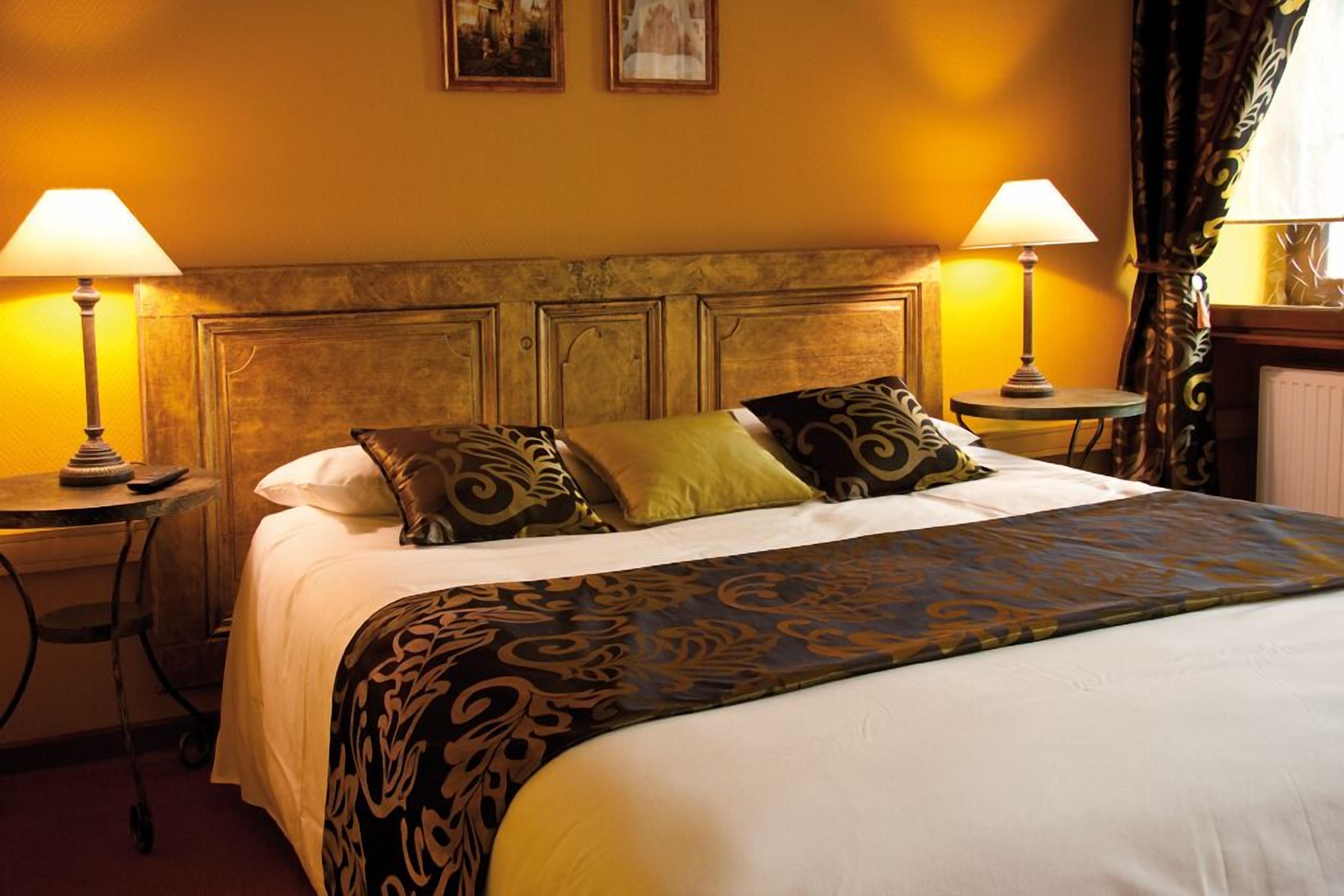 A hotel room with a large bed, two bedside tables with lamps, a headboard, and a window with curtains.