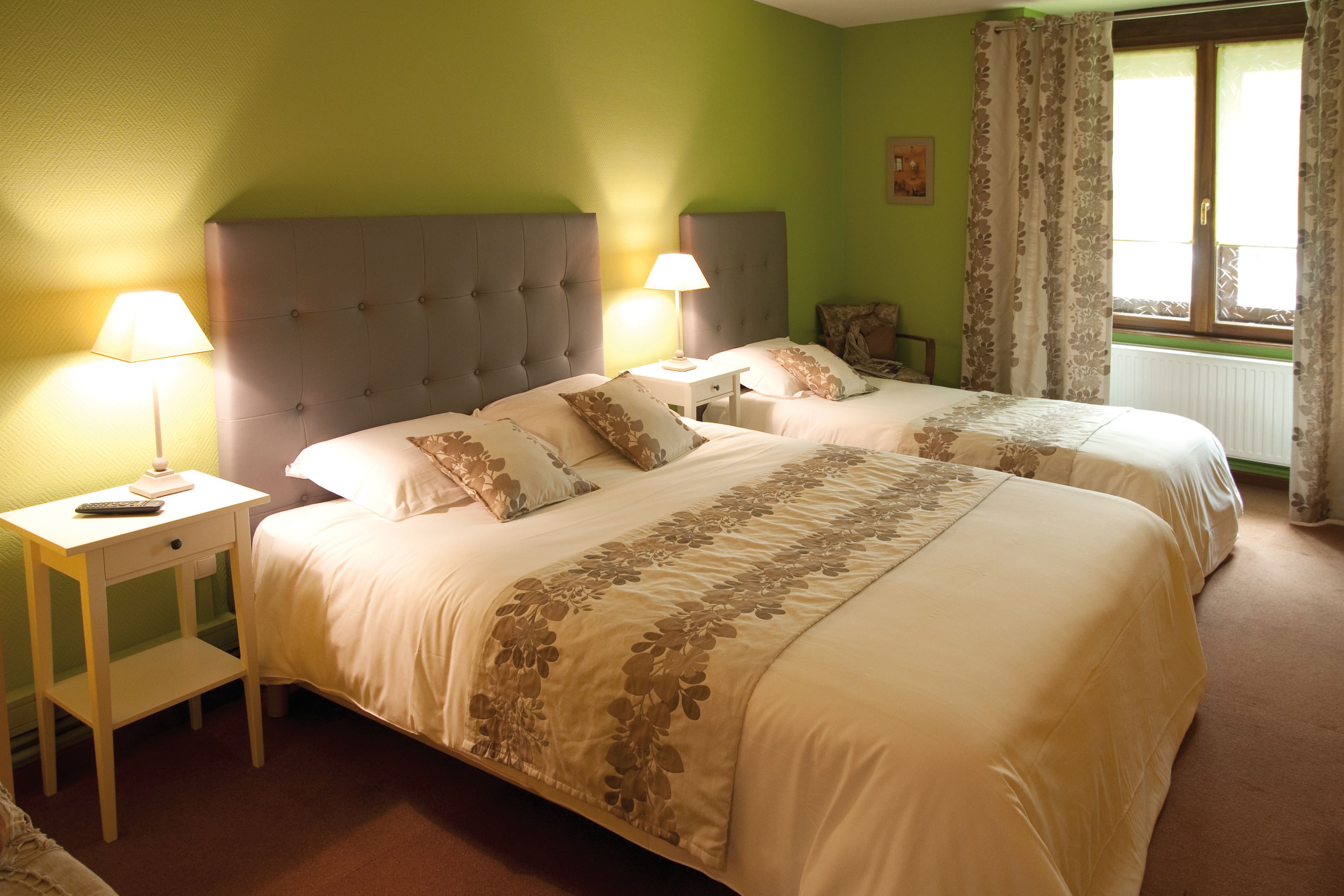 Une chambre d’hôtel avec deux lits, chacun doté d’une table de chevet et d’une lampe, une fenêtre avec des rideaux et un radiateur.