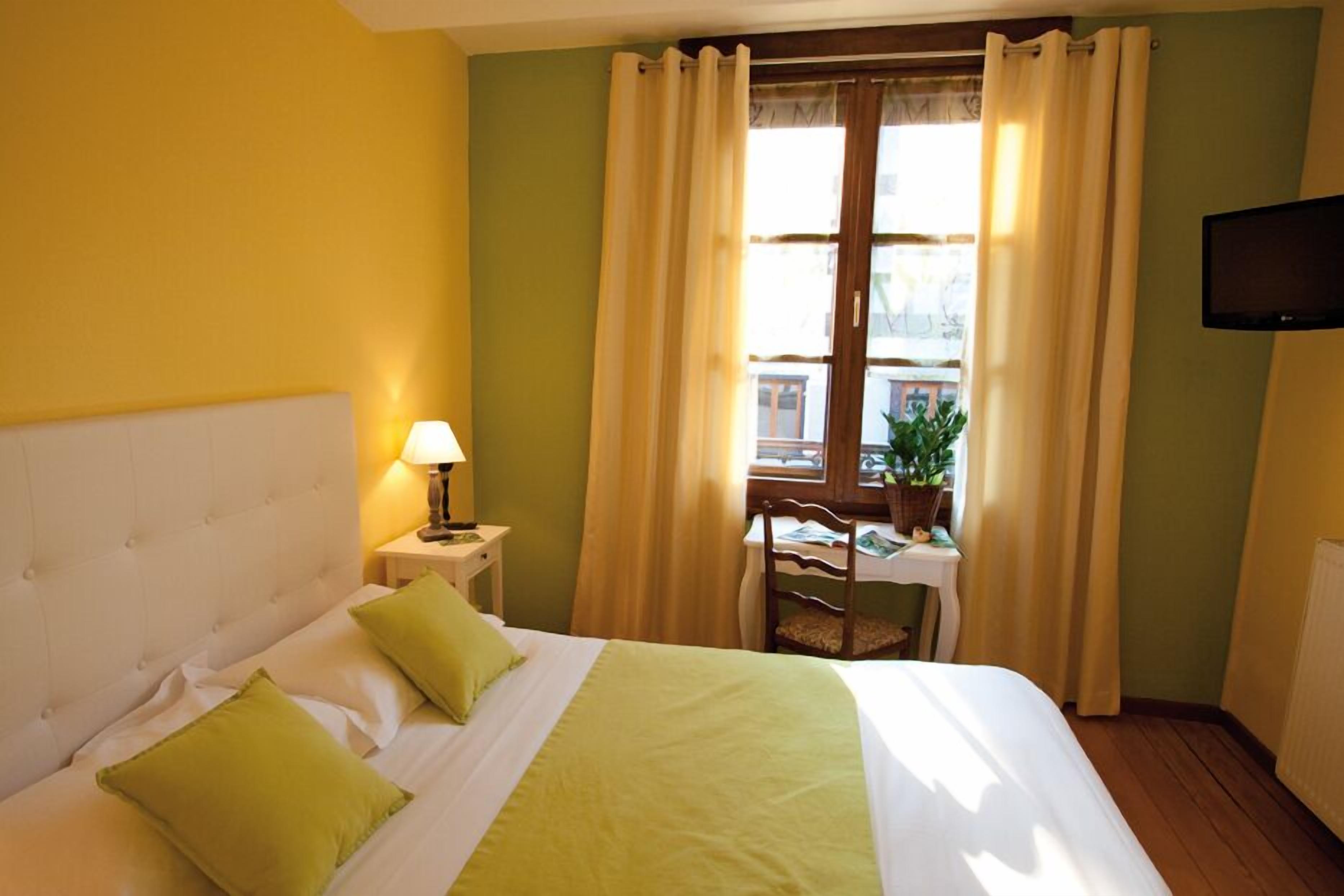 Una camera d'albergo con un letto, un comodino con una lampada, una sedia, un tavolo con una pianta e una TV montata a parete.