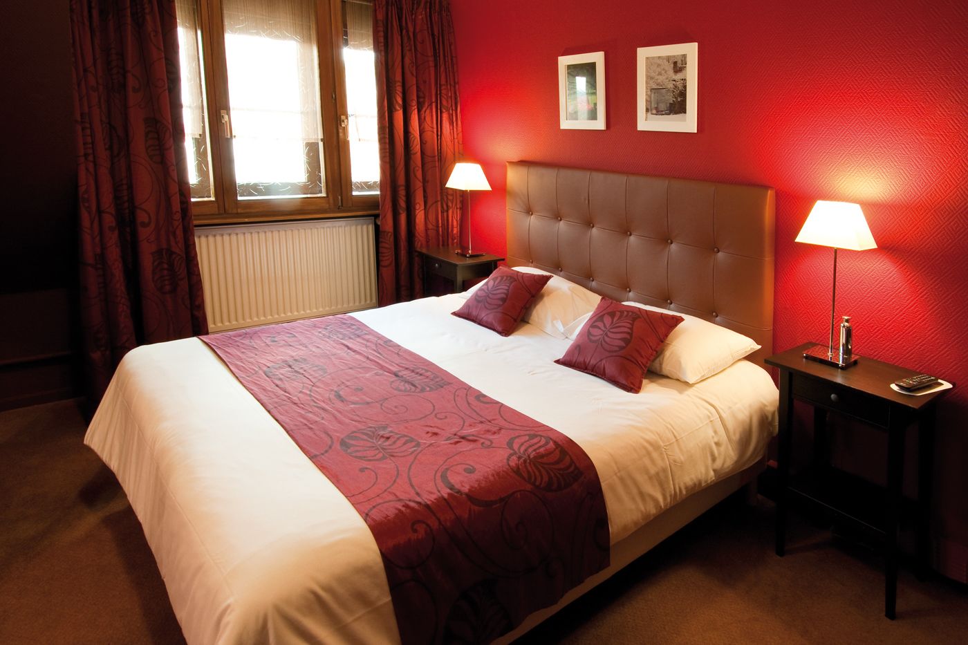 Habitación de hotel con una cama grande, dos lámparas de noche, una ventana con cortinas y dos cuadros en la pared.