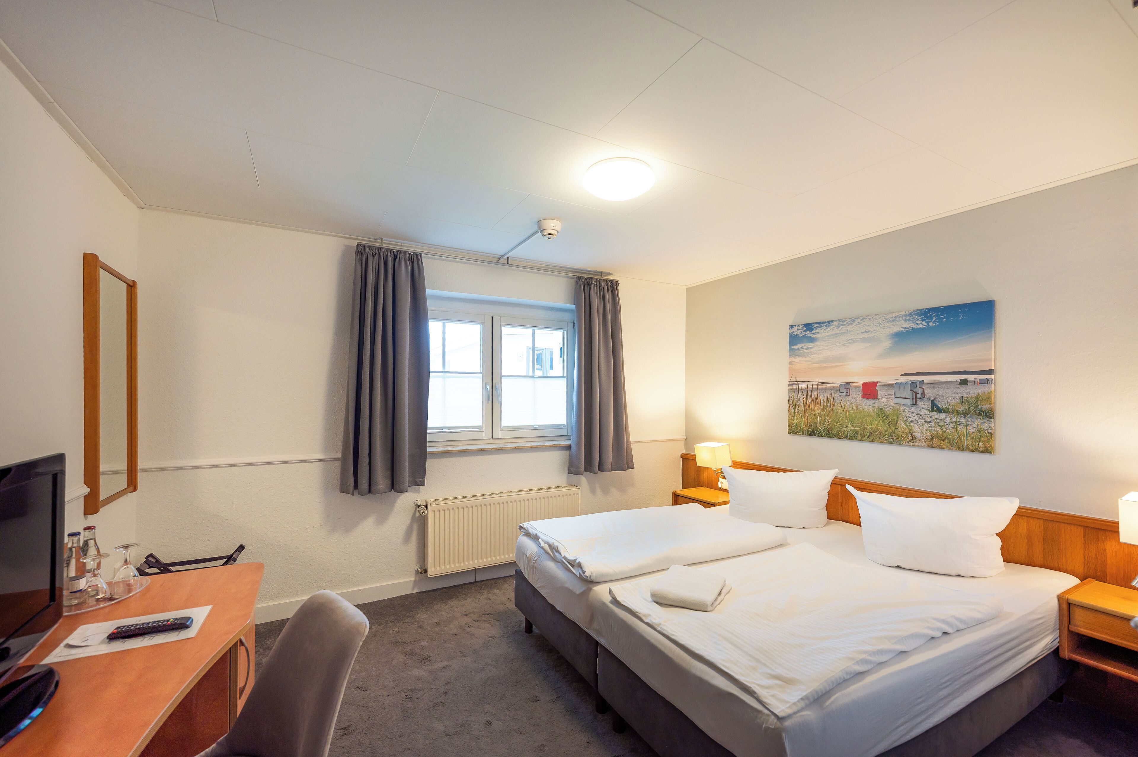 A hotel room with two beds, a desk, a TV, and a window with curtains.