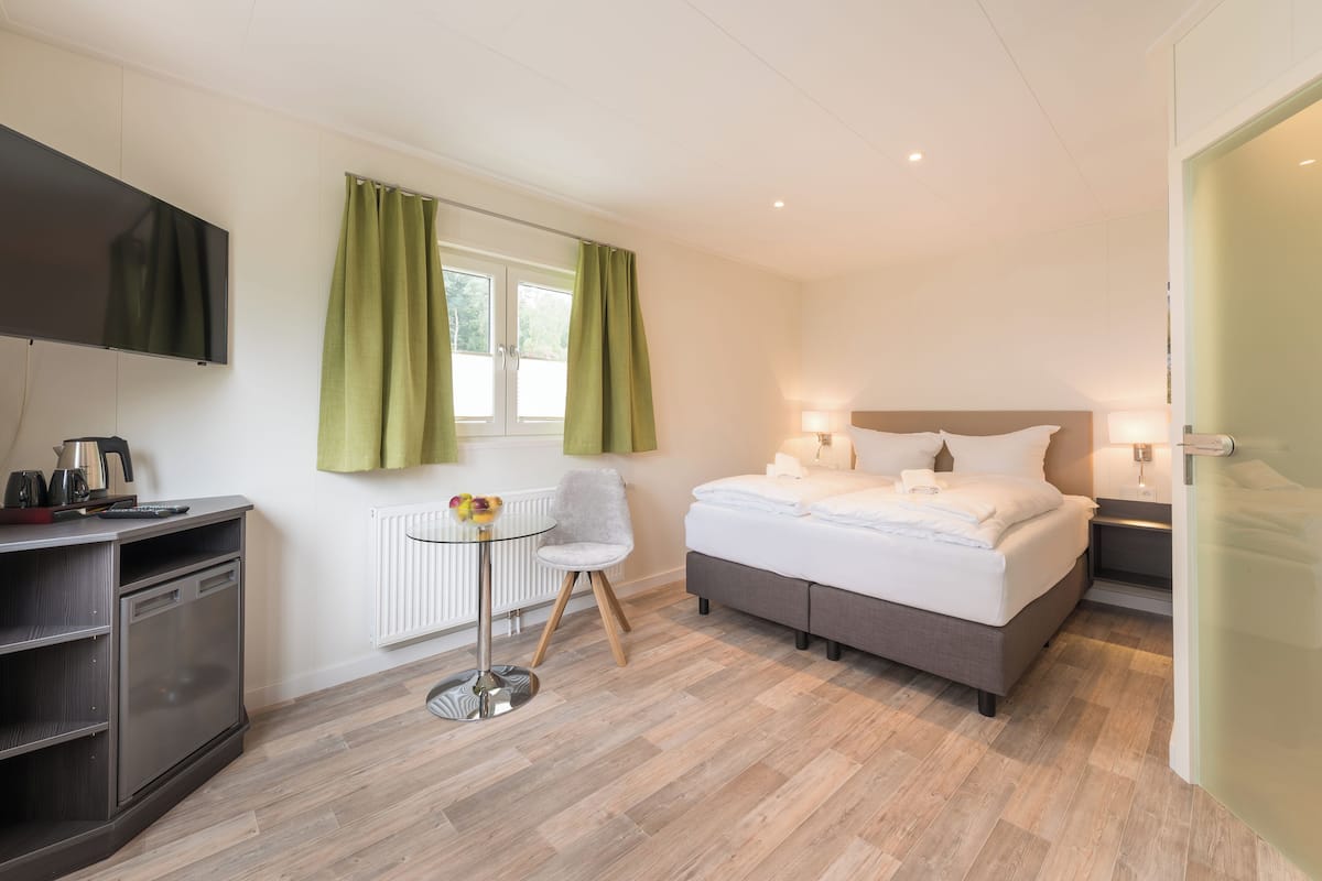 A modern hotel room with a bed, bedside table, lamp, TV, and a small table with a chair.