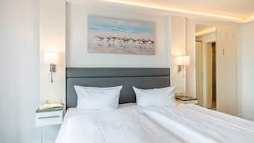 A hotel room with a large bed, two bedside tables, a nightstand, a painting of birds on the wall, and a door leading to another room.