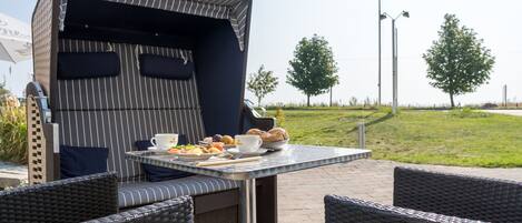 An outdoor dining area with a grill, wicker furniture, and a flag in the background.