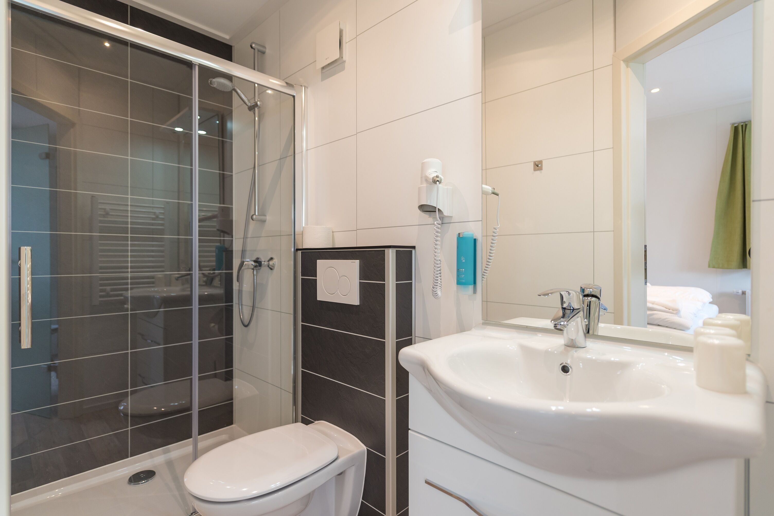 A modern bathroom with a glass shower enclosure, a white toilet, a sink with a mirror, and a towel rack.