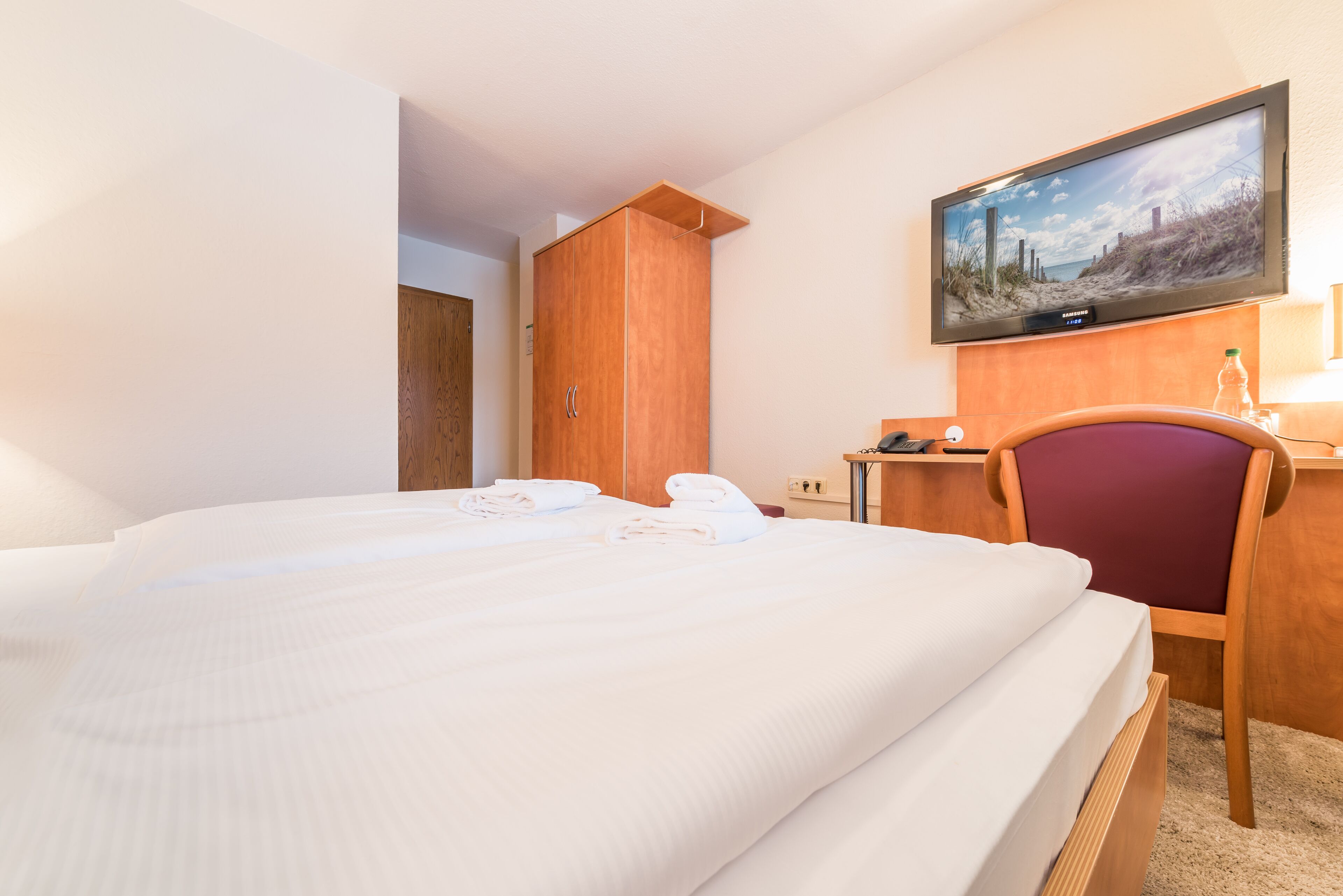 Ein Hotelzimmer mit einem Bett, einem Holzschrank, einem Schreibtisch mit Stuhl und einem an der Wand befestigten Fernseher.
