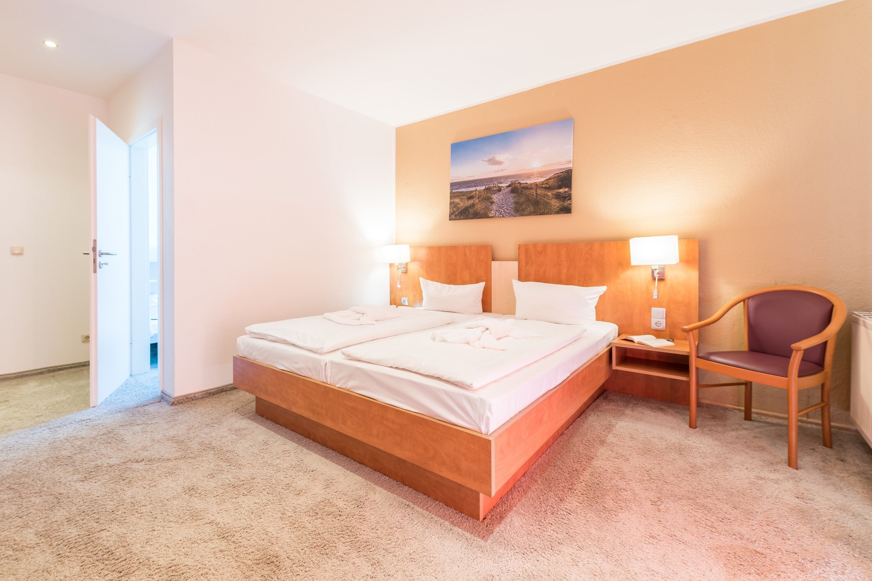 Un dormitorio con una cama de madera, dos mesitas de noche, una silla y un cuadro en la pared.