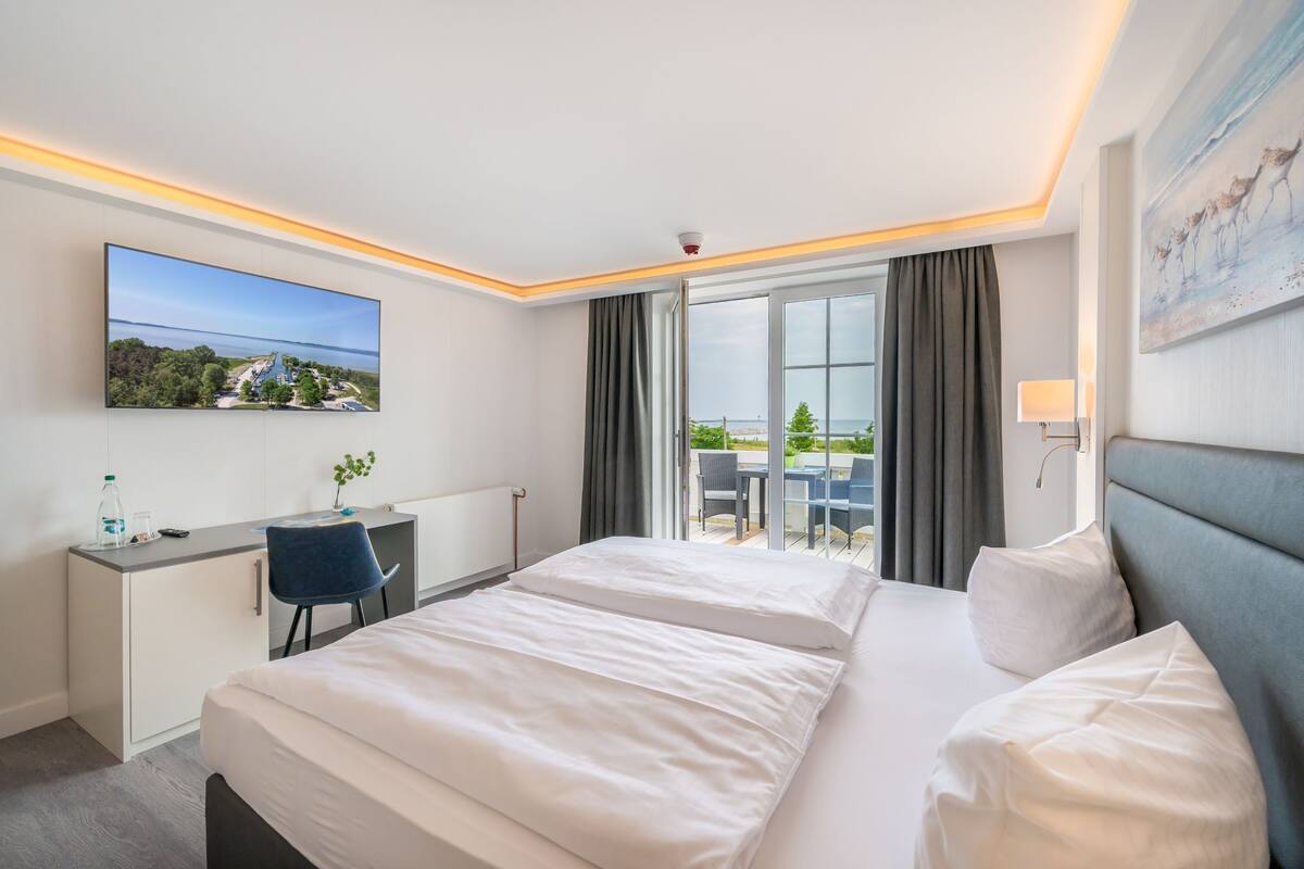 A hotel room with a bed, desk, and a large window offering a view of the outdoors.