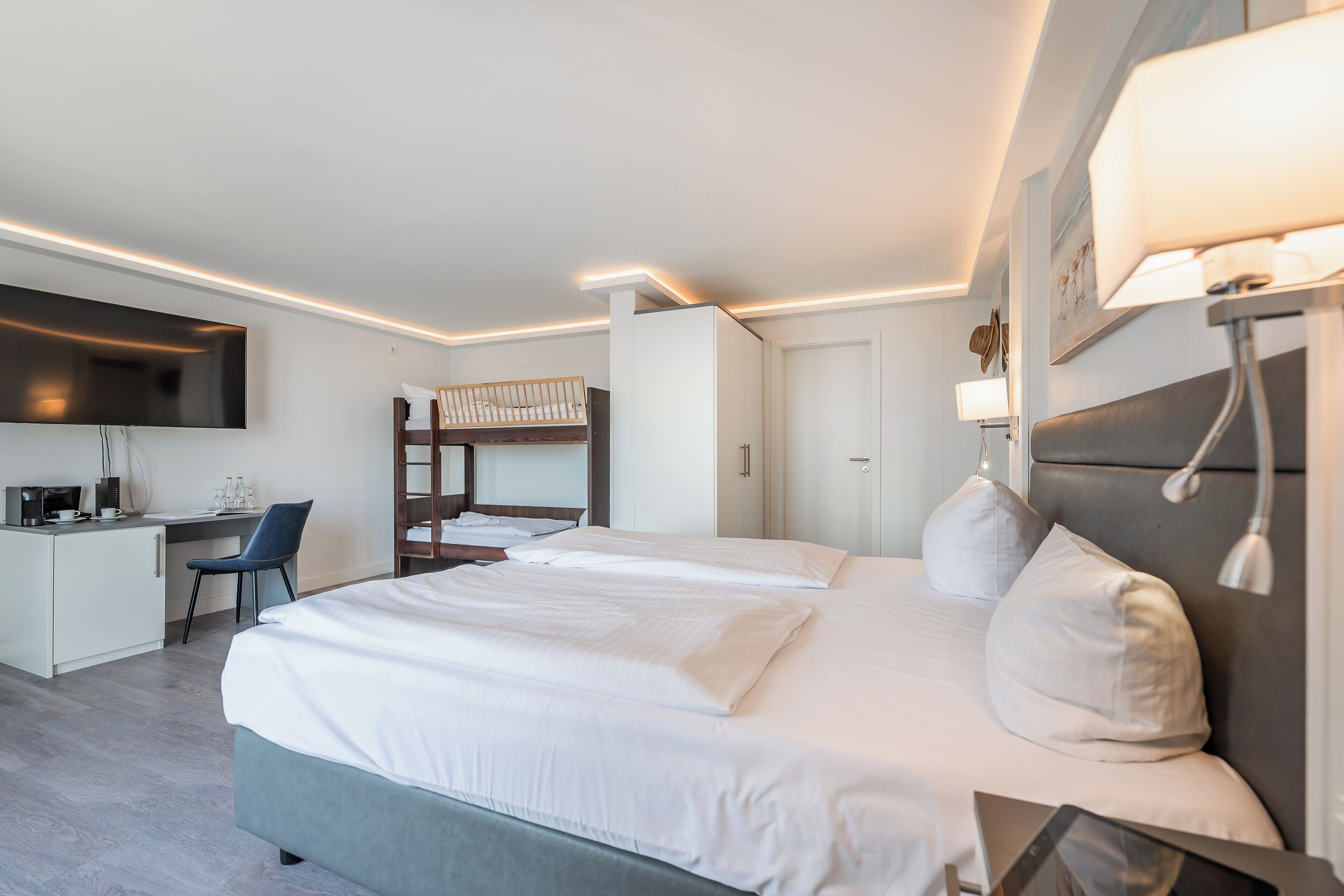 Ein modernes Hotelzimmer mit einem großen Bett, einem Schreibtisch, einem Etagenbett und einem Flachbildfernseher.