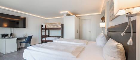 A modern hotel room with a large bed, a desk, a bunk bed, and a flat-screen TV.