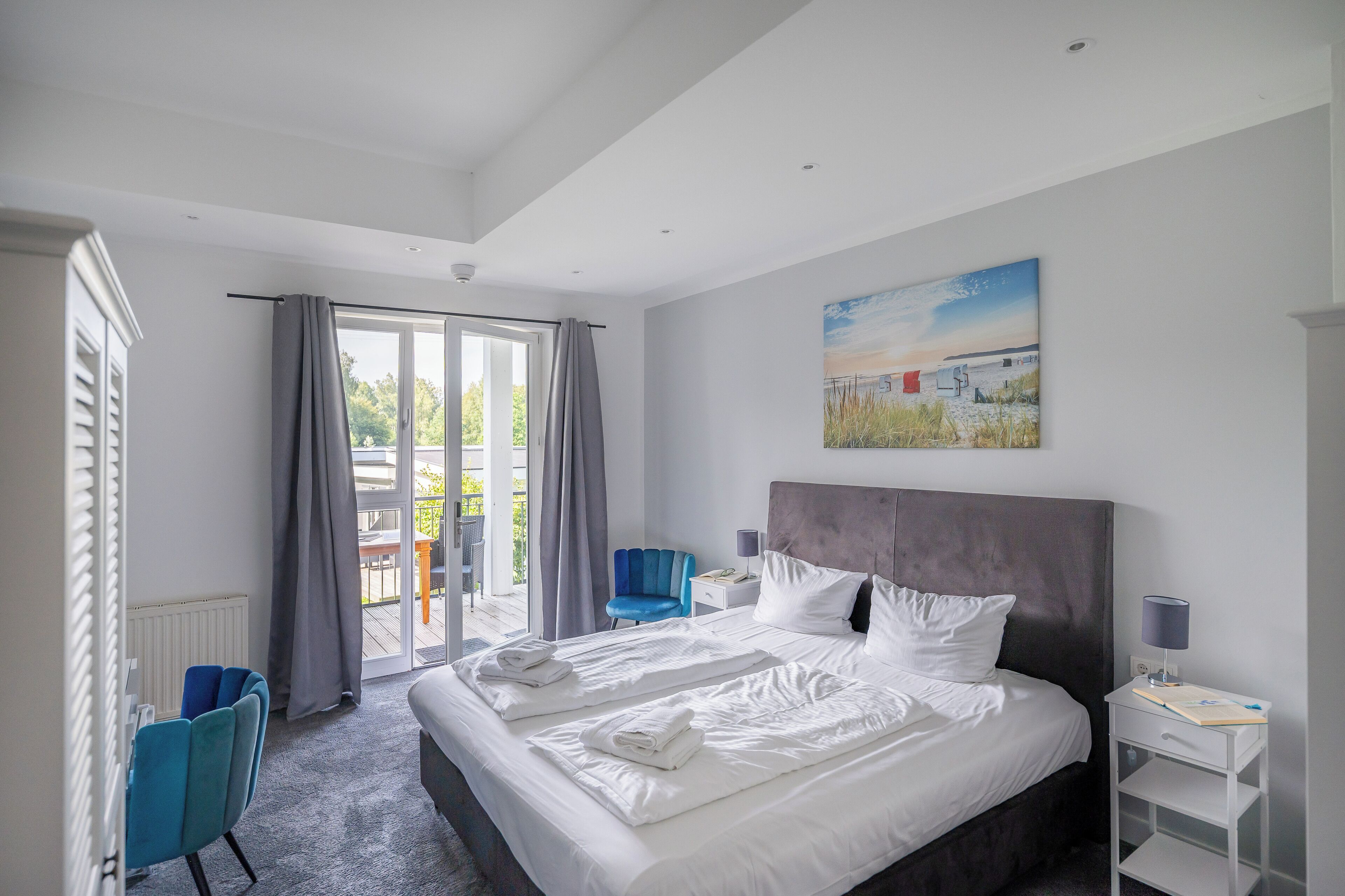 Moderni hotellihuone, jossa on suuri sänky, sininen tuoli, työpöytä lampun kanssa ja näkymä ulos.