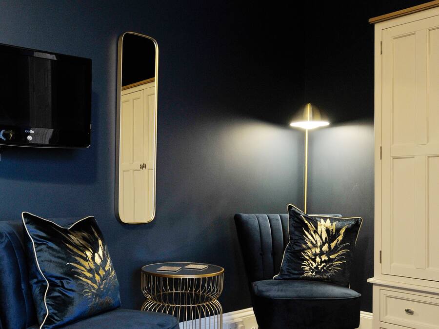 A room with two dark blue armchairs, a round side table, a floor lamp, a TV mounted on the wall, and a white cabinet.