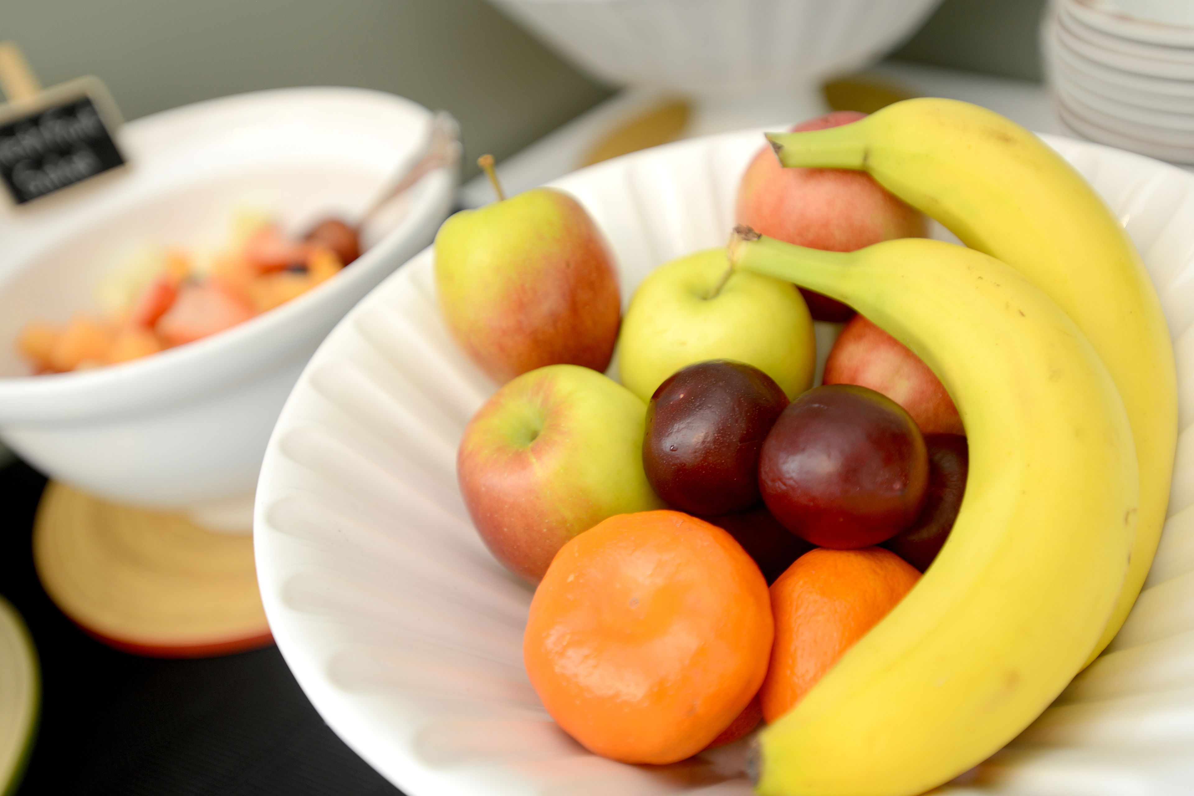 A white bowl containing a variety of fruits including apples, bananas, and plums.
