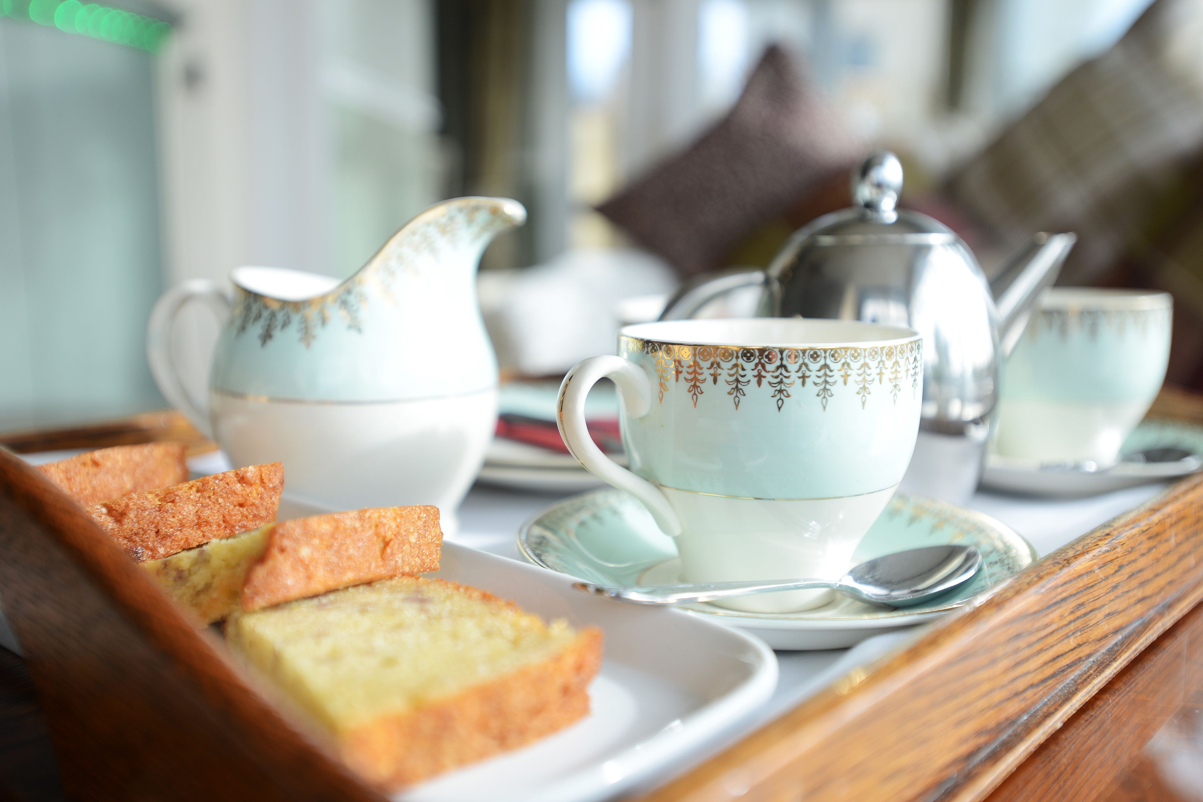 A tray with a teapot, cups, saucers, and slices of cake on a wooden table.