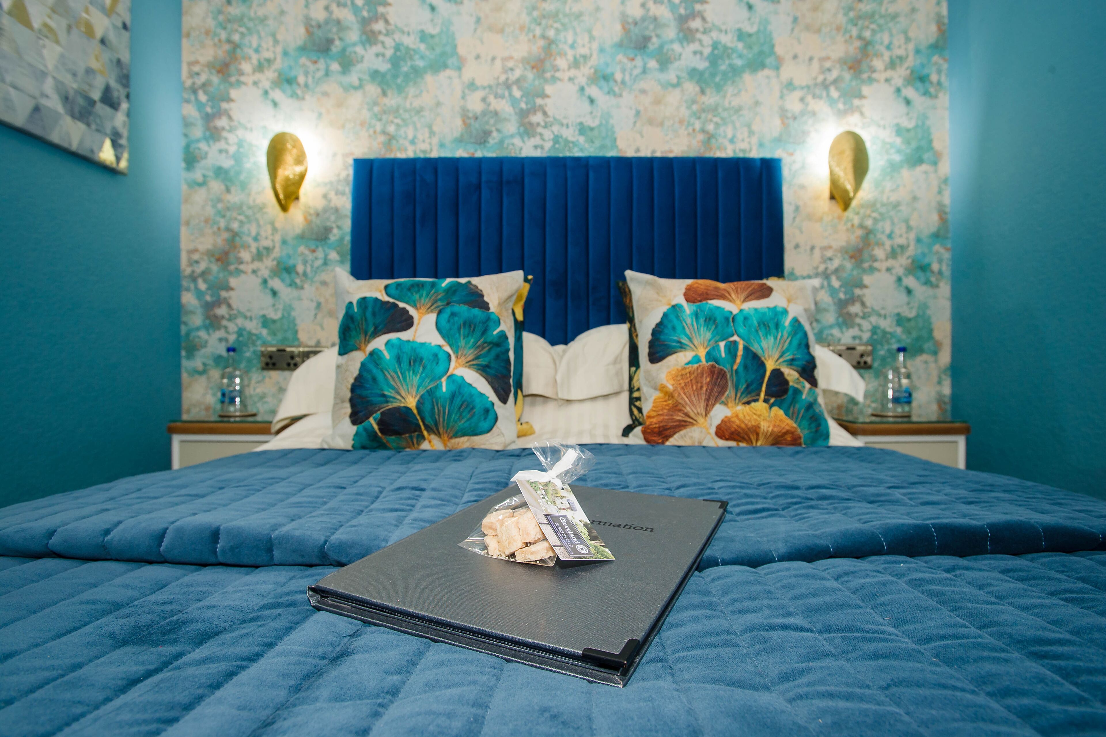 A neatly made bed with a blue quilt, a pillow with a floral design, and a small package on the bed.