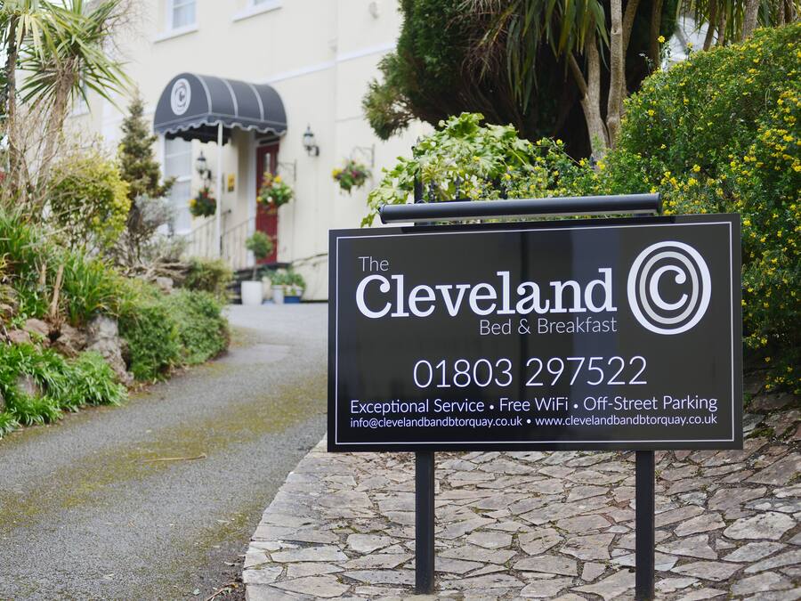 A sign for The Cleveland Bed & Breakfast, featuring a contact number and amenities like exceptional service, free WiFi, and off-street parking.