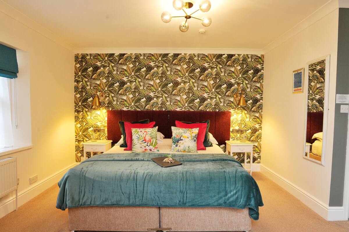 A bedroom with a large bed, floral wallpaper, and a chandelier.