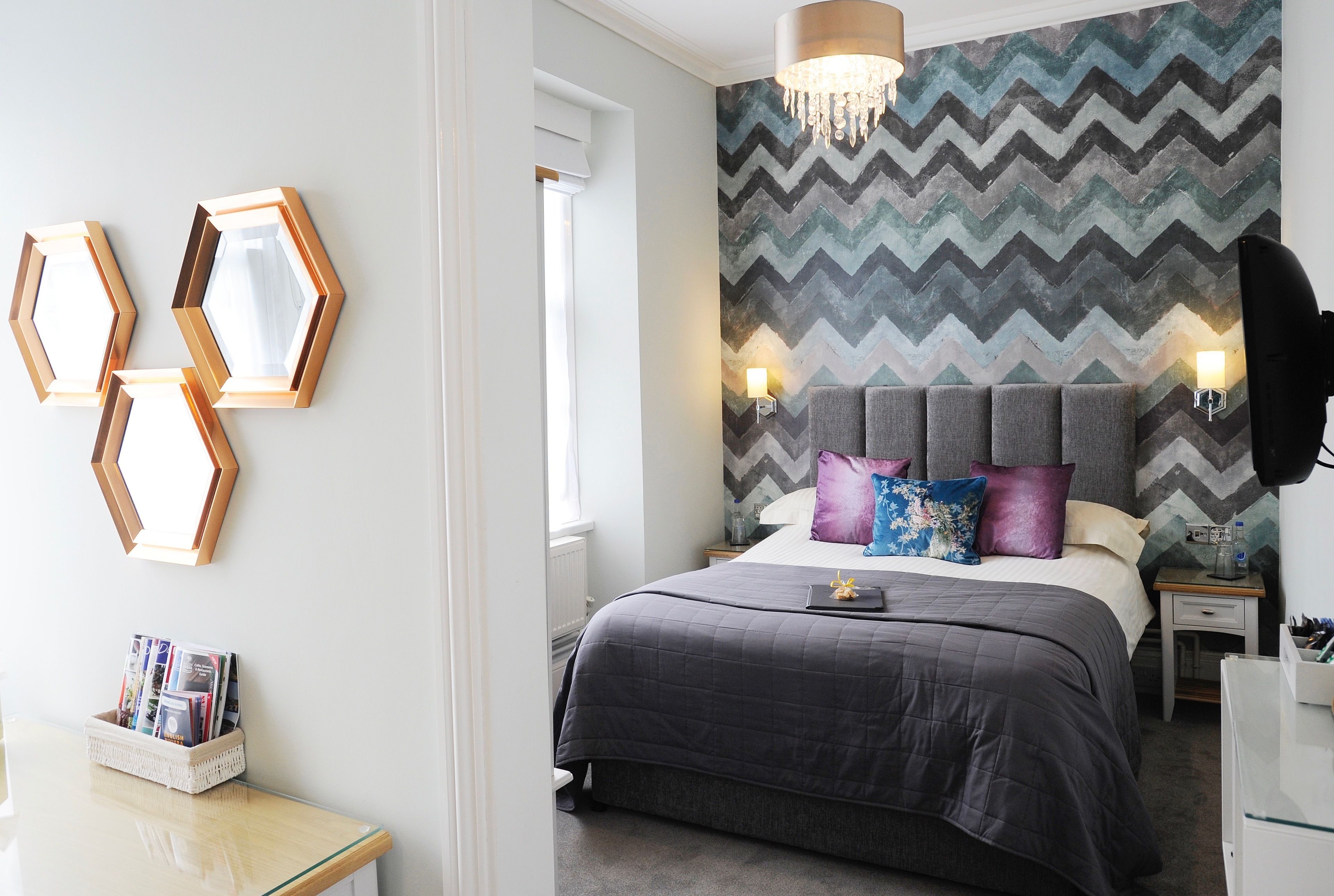 Une chambre à coucher comprenant un lit, une table de chevet, un téléviseur fixé au mur et un mur décoratif orné d’un motif en zigzag.