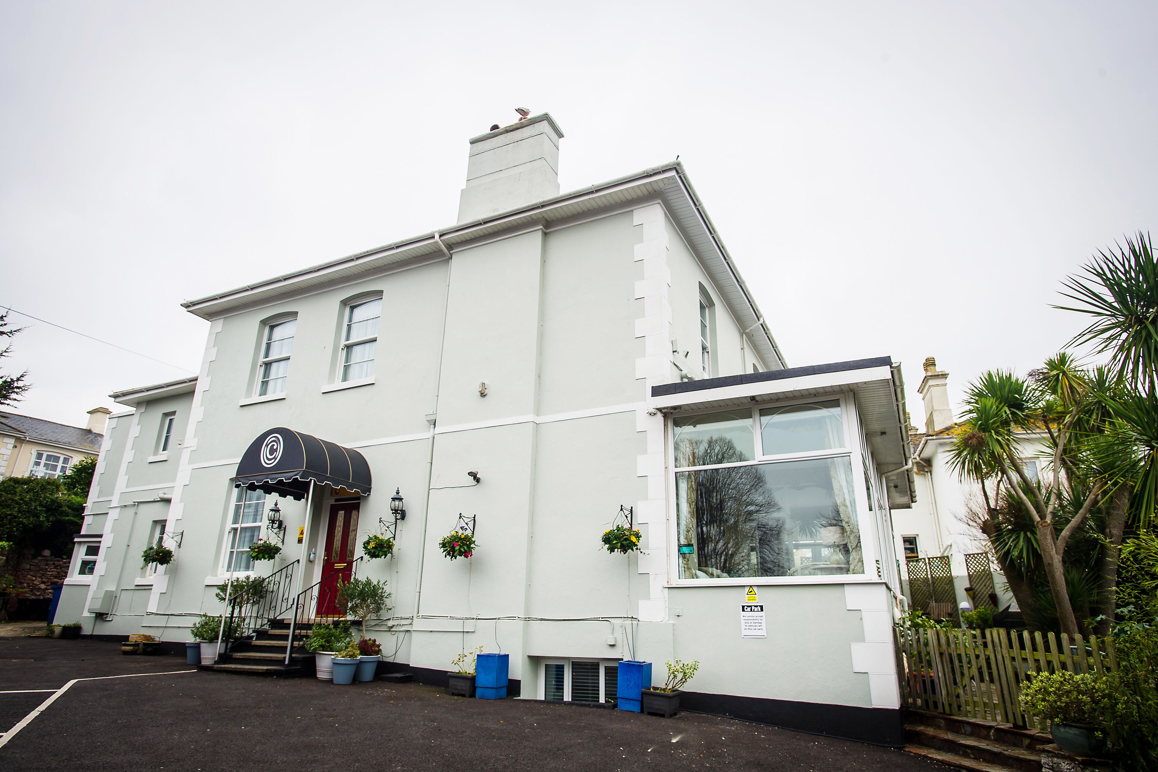 A white building with a black awning, a red door, and hanging flower baskets.